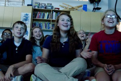 A group of students sitting on the floor watching a live science show during their field trip or group visit.